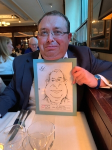 Francis Ingham having lunch with Richard Bagnall joking with his caricature from the Malaysia PR Summit 2019